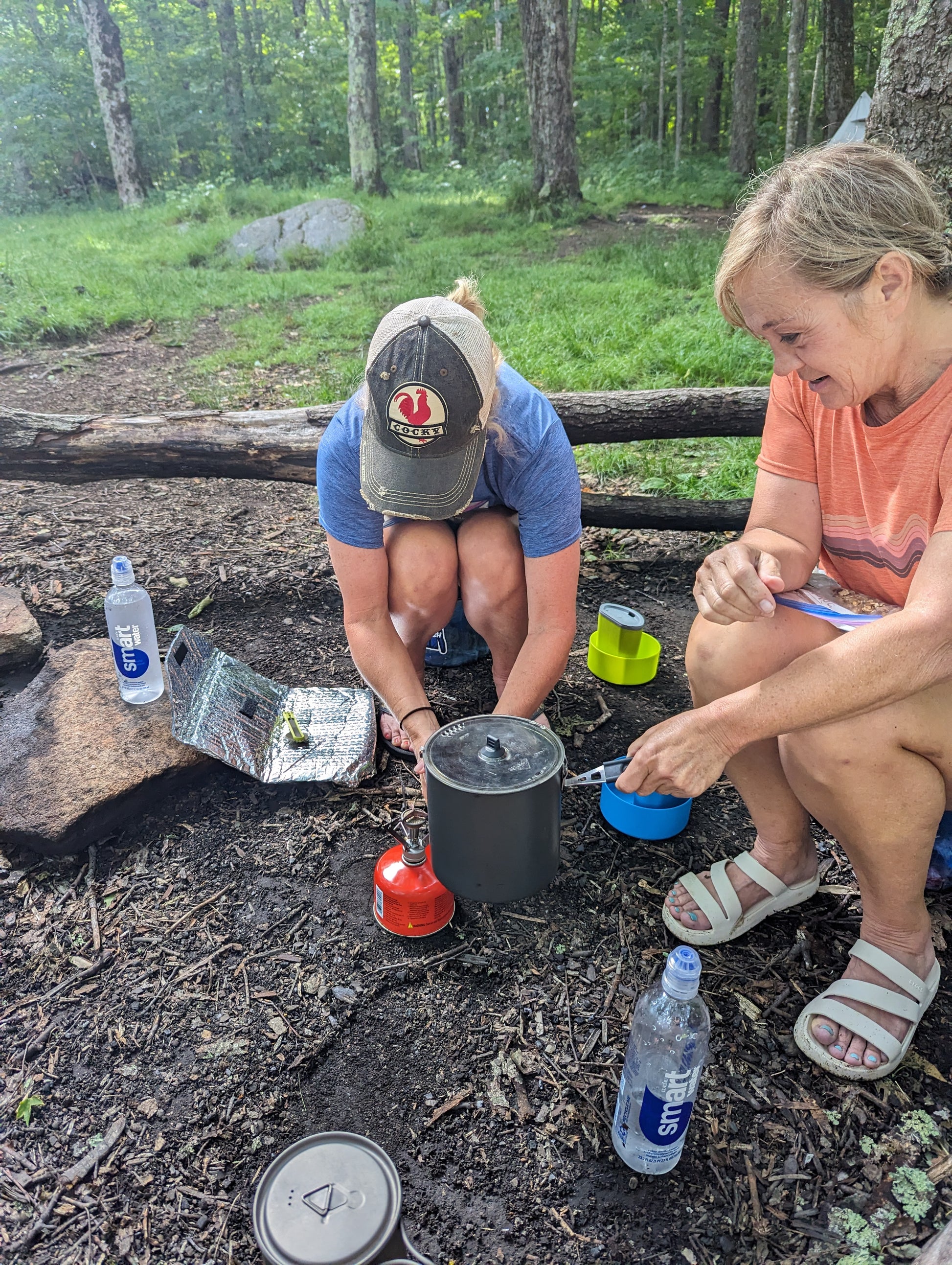 Two women heating water in a backpacking stove while sitting at a campsite