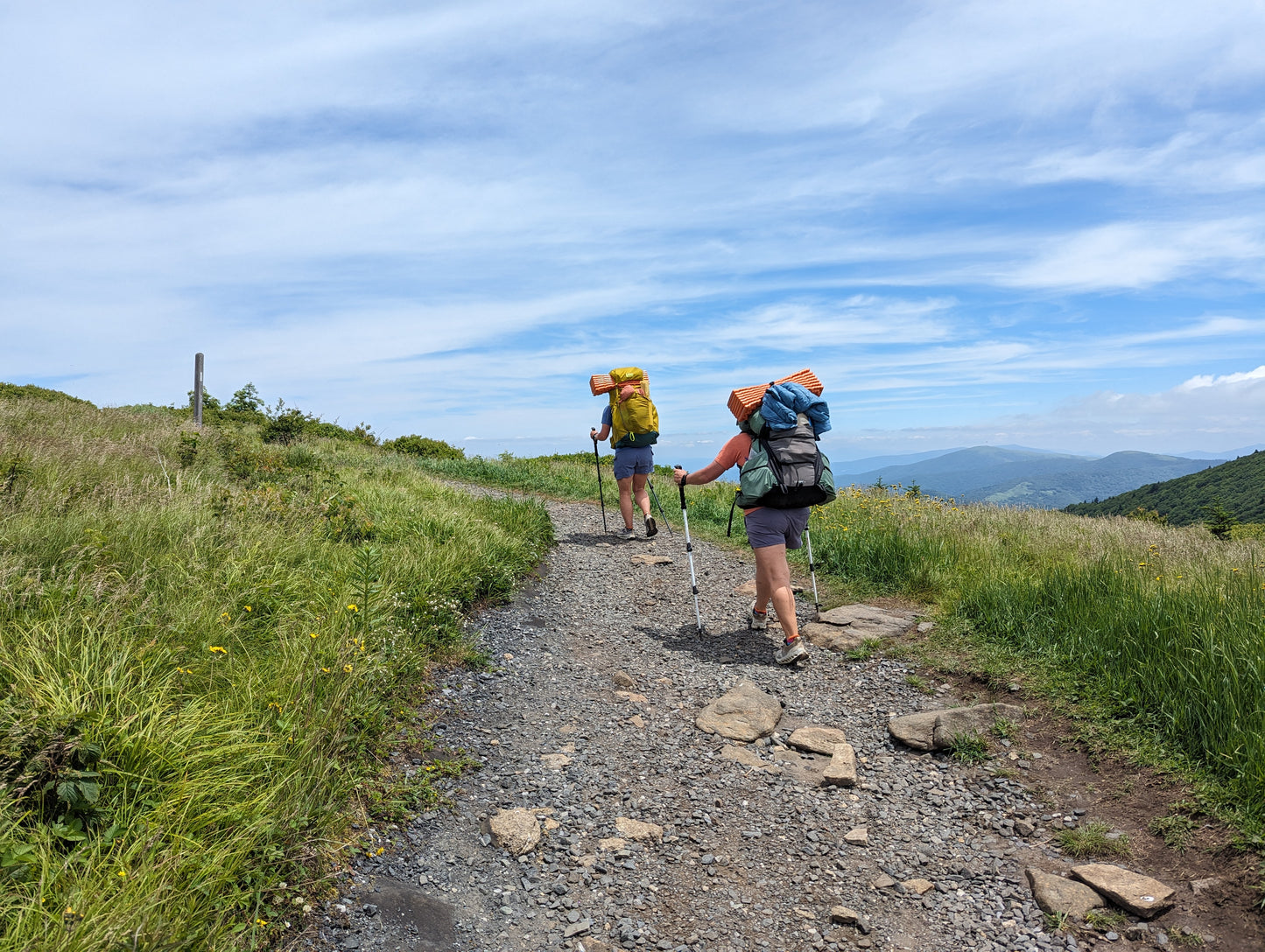 Two hikers ascending a rocky trail with mountains in the background