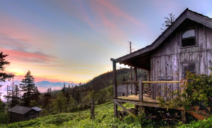 A rustic cabin on top of a mountain with the sun setting in the background