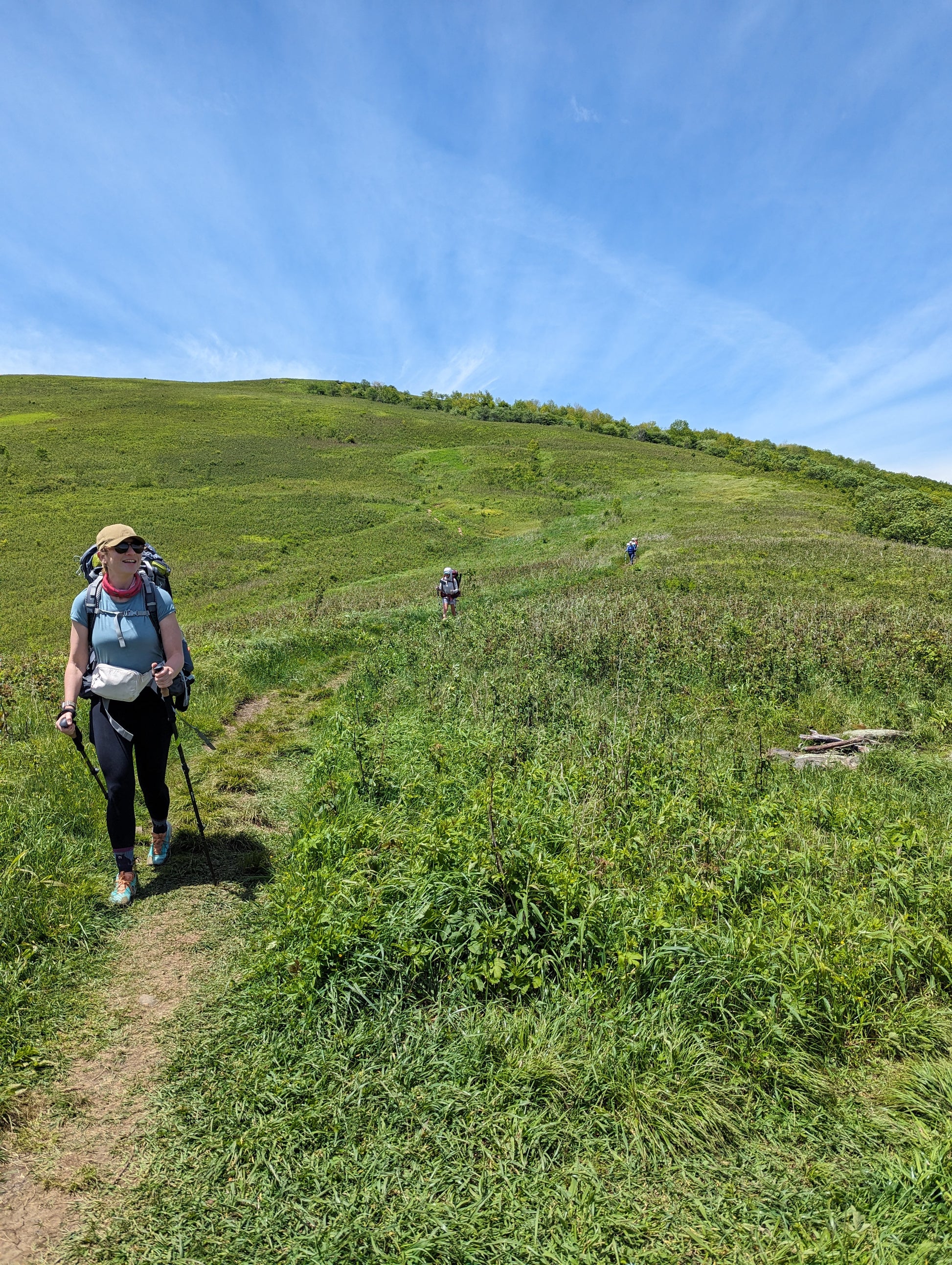 A woman hiking on a trail through a grassy meadow