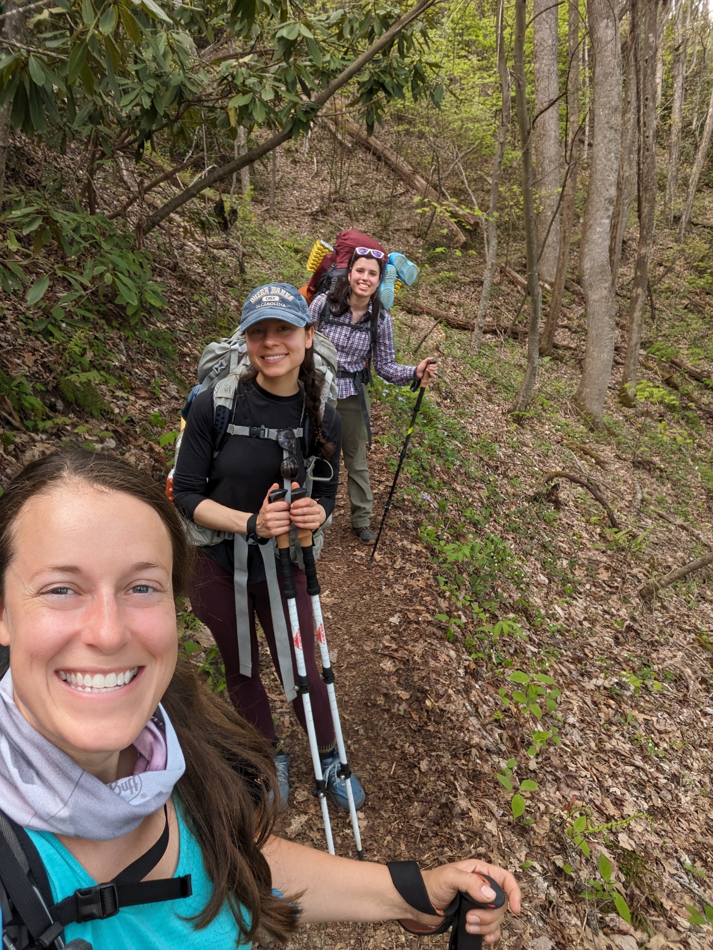 Three women smiling while backpacking on a hiking trail